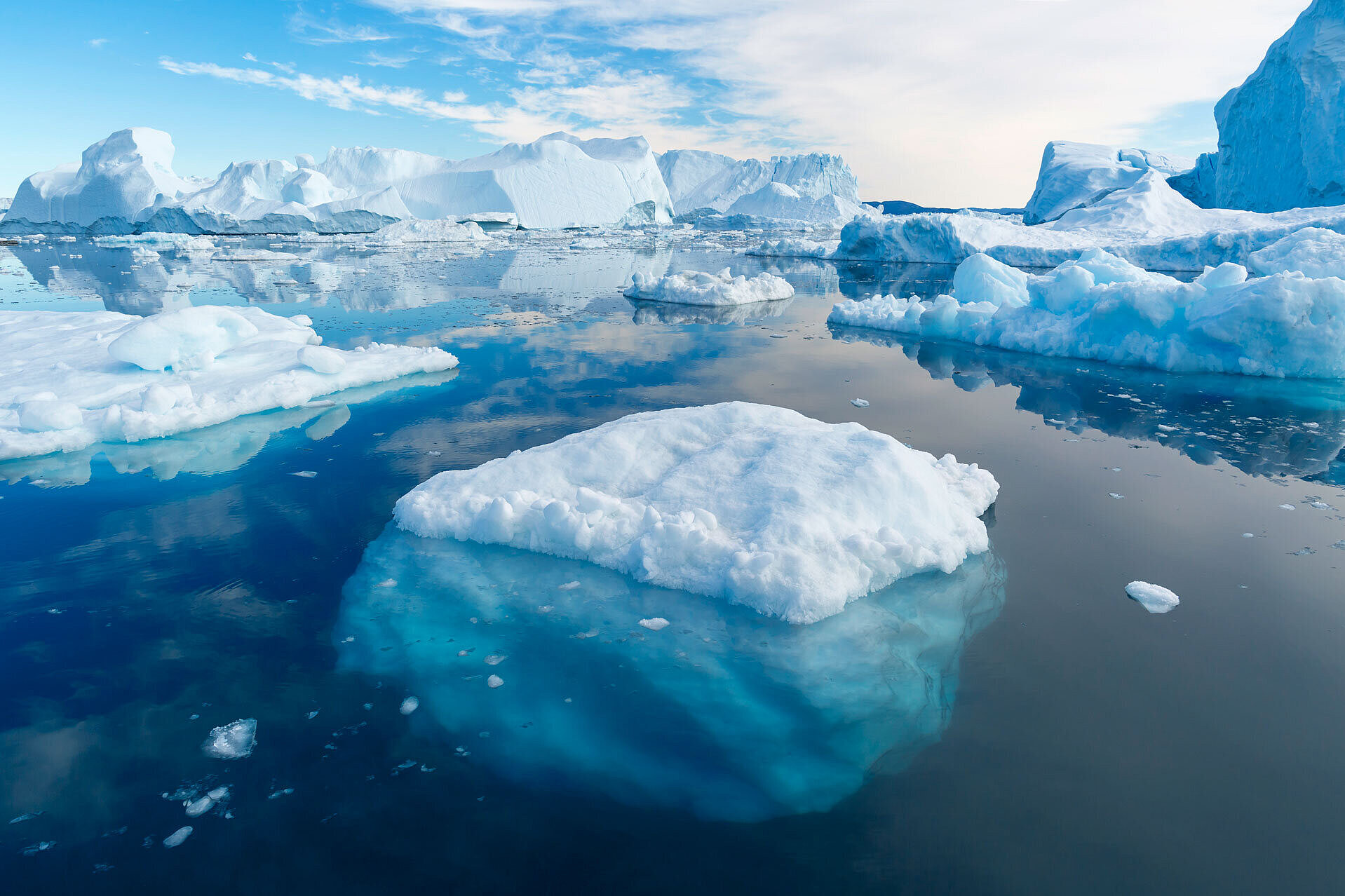 Schwimmende Eisschollen und Eisberge im offenen Meer unter blauem Himmel als Symbolbild für den Klimawandel.